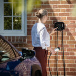 Lady operating EV charger with blue car