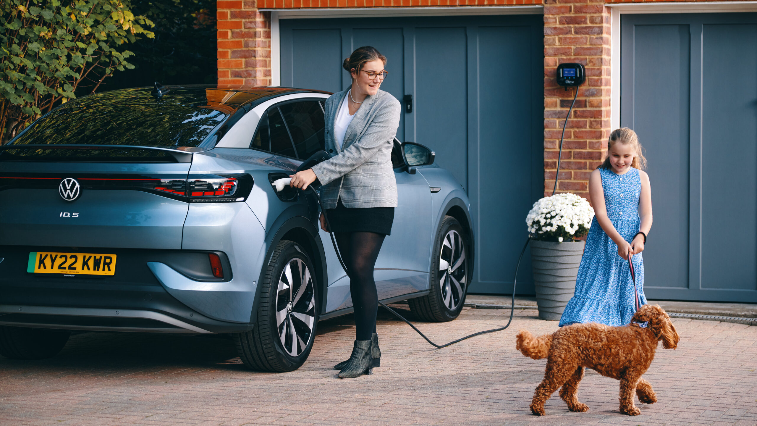 Lady with child and dog plugging in Volkswagen ID5 EV to Ohme EV charger