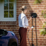 Lady using EV charger to plug in blue electric car