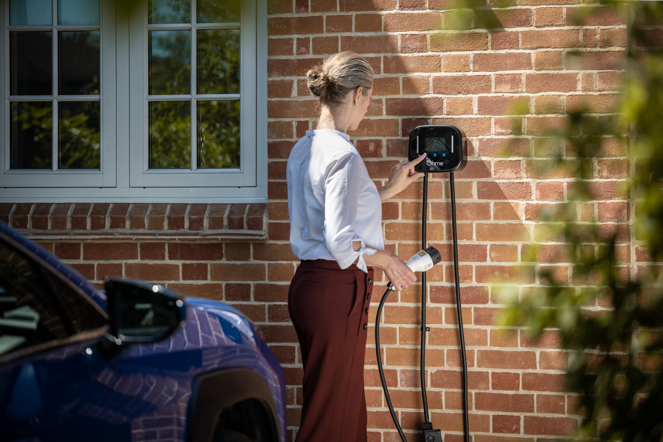 Lady using EV charger to plug in blue electric car