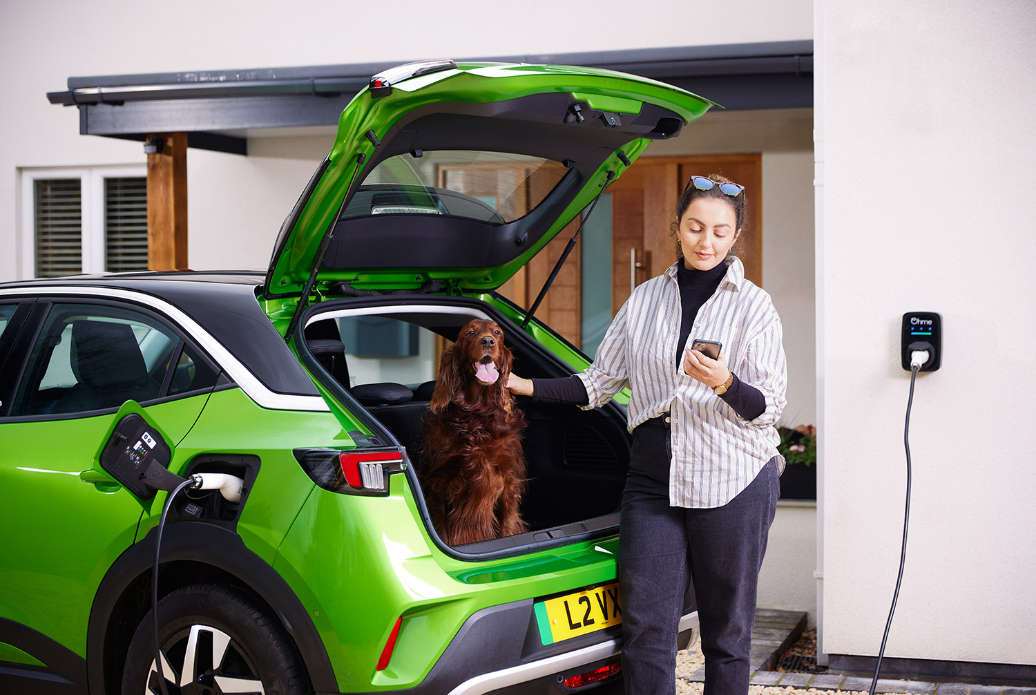 Green Vauxhall Mokka EV being charged with lady and red setter