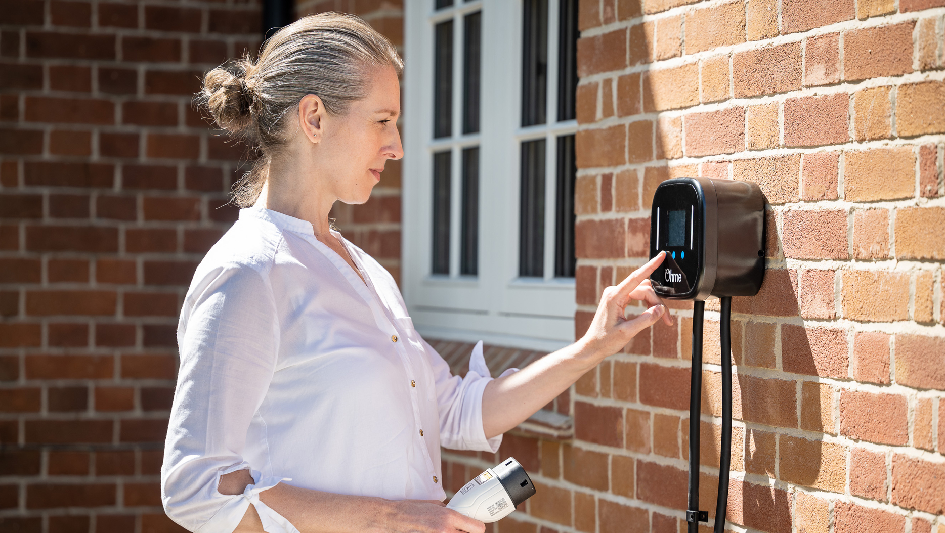 Person using the Ohme Home Pro charger installed on a brick wall