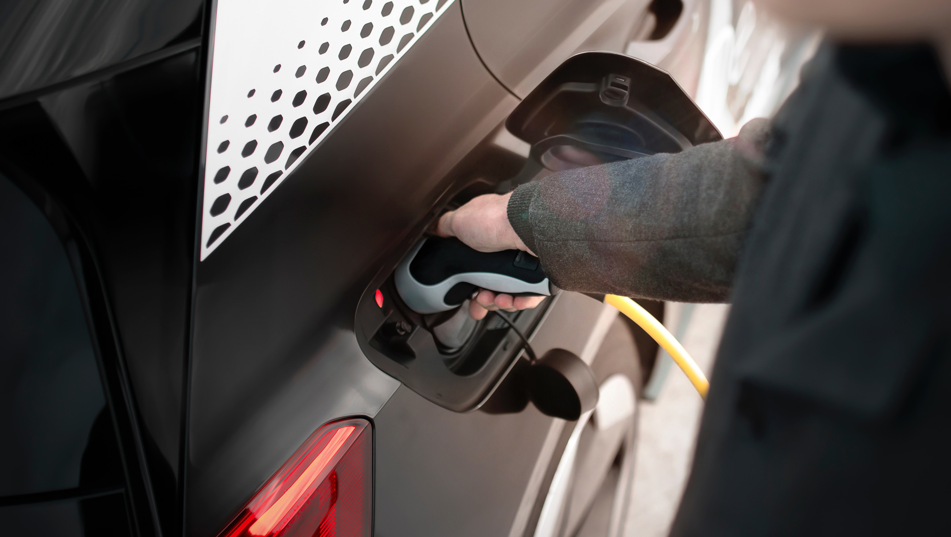 Person plugging a charging cable into an electric vehicle