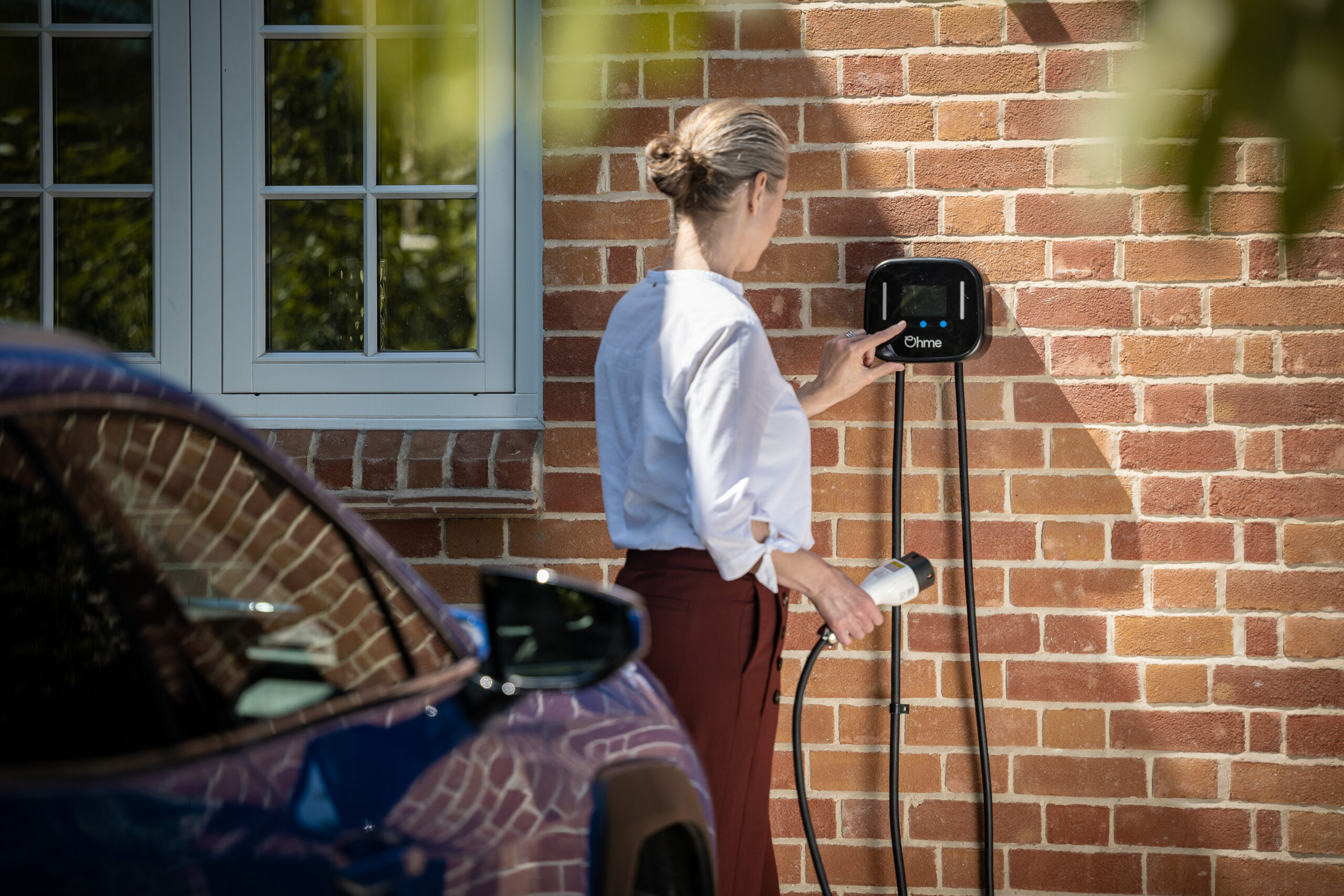 Lady operating EV charger with blue car